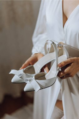 Sabahları beyaz bir bornozla inanılmaz güzel bir gelin ve yatak odasında uzun bir peçe ve elinde ayakkabılar. Gelin sabah poz verir..