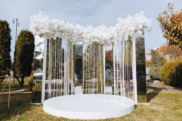 Düğünde dekorasyon. Beyaz çiçeklerle süslenmiş ve ağaç zeminine kurdele asılmış bir kemer. Kutlama için her şey hazır. Düğün..