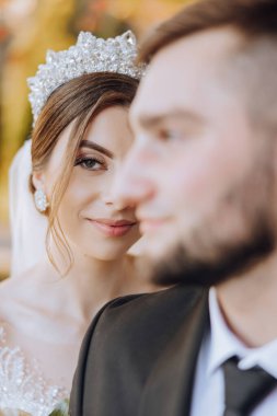 Elinde bir buket çiçekle kameraya bakarken kocasına sarılan gülümseyen bir gelinin portresi. Güzel bir düğün kutlaması. Duvağı olan düğün saç stili. Birbirine aşık çift.