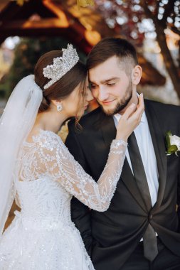 Güzel ve şık yeni evliler güzel bir bahçede sonbahar doğasının arka planına karşı sarılıp gülümsüyorlar. İnanılmaz güzel genç bir gelin, sevgili damadının omzuna yaslandı.