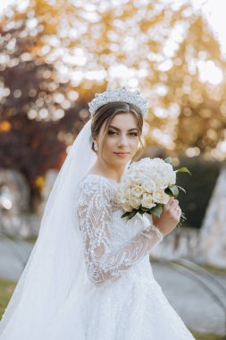 Portre. Elbise ve duvak takmış esmer bir gelin şık bir taç poz verir ve buketini koklar. Gümüş mücevherler. Güzel makyaj ve saç. Sonbahar düğünü. kutlama