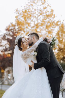 Genç bir gelin ve damat sonbahar güneşinin ışınlarında şefkatle kucaklaşır. Şefkatli ve güzel genç kız gelin. Bir adam sevgilisini öper. Güzel bir bahçenin arka planında