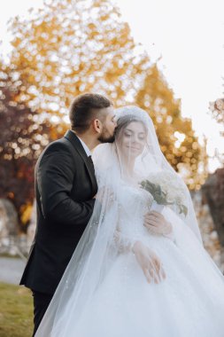 Sonbahar parkında yürüyüş yapan düğün çifti. Güzel beyaz elbiseli gelin. Aşk ve ilişki kavramı. Doğada damat ve gelin