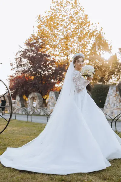 Düğün fotoğrafı. Dantelli, dolgun elbiseli esmer bir gelin elinde bir buket tutarak bahçede yürüyor, içtenlikle gülümsüyor. Harika saç ve makyaj. Moda ve tarz. Kutlama.