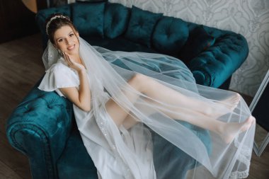 Sabahları beyaz bir bornozla inanılmaz güzel bir gelin ve yatak odasındaki yatakta uzun bir peçe oturuyor. Gelin, düğün töreninden önce poz verir..