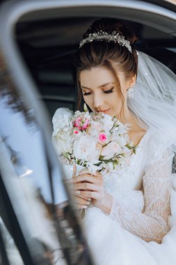 Gelin elinde bir buket çiçekle siyah bir arabada oturuyor ve arabadan dışarı bakıyor. Arabada utangaç bir gelinin portresi. Gelin, gülümse, duygular.
