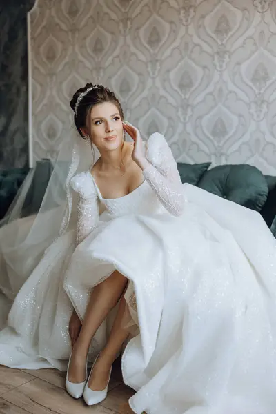 Young bride in beautiful wedding dress putting on shoes indoors. Bride dresses shoes before the wedding ceremony. Detail of bride putting on high heeled sandal wedding shoes. Wedding bride shoes.