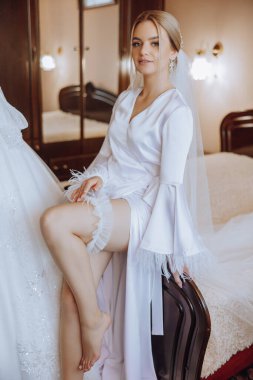 Sabahları beyaz bir bornozla inanılmaz güzel bir gelin ve yatak odasındaki yatakta uzun bir peçe oturuyor. Gelin, düğün töreninden önce poz verir..