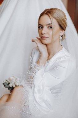 Yatak odasında beyaz bornozlu inanılmaz güzel bir kızın portresi. Gelin düğün töreninden önce sabah poz veriyor..