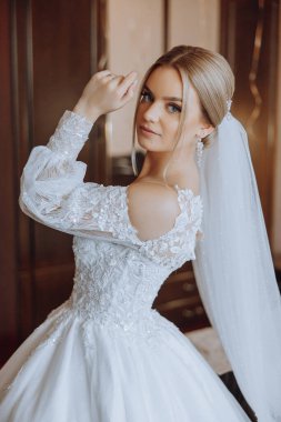 Şık bir gelinlik içinde sarı saçlı ve düğün sabahı odasında çarpıcı makyajlı güzel bir gelinin moda fotoğrafı. Gelin düğün için hazırlanıyor.