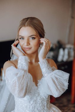 Şık bir gelinlik içinde sarı saçlı ve düğün sabahı odasında çarpıcı makyajlı güzel bir gelinin moda fotoğrafı. Gelin düğün için hazırlanıyor.