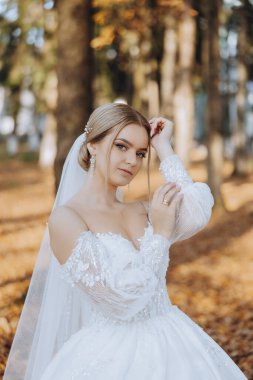 Düğün portresi. Sarışın, dantelli, omuzları açık, doğada poz veren bir gelin. Güzel saç ve makyaj. Sonbahar. Gün ışığı. kutlama.