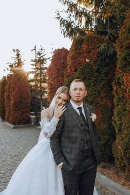 Güzel ve şık yeni evliler güzel bir bahçede sonbahar doğasının arka planına karşı sarılıp gülümsüyorlar. İnanılmaz güzel genç bir gelin, sevgili damadının omzuna yaslandı.