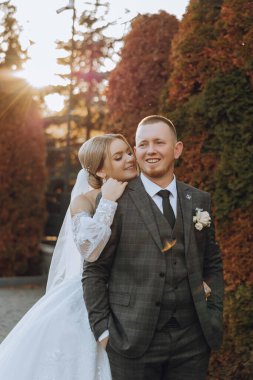 Güzel ve şık yeni evliler güzel bir bahçede sonbahar doğasının arka planına karşı sarılıp gülümsüyorlar. İnanılmaz güzel genç bir gelin, sevgili damadının omzuna yaslandı.