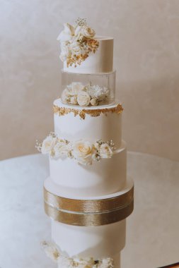 Ziyafet salonunda büyük lüks, çok katmanlı bir düğün pastası taze beyaz gül çiçekleriyle süslenir. Akşam ışığında düğün tatlısı. Düğün dekoru.