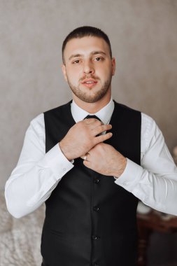 Beyaz gömlekli genç bir adam odanın penceresinin yanında duruyor ve kravat takıyor. Damat sabah giyinir ve düğün için hazırlanır..