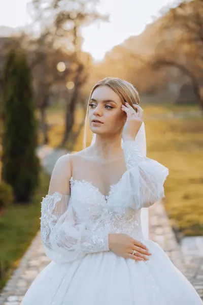 Wedding portrait. Blonde bride in a lace dress with open shoulders, posing in nature. Beautiful hair and makeup. Autumn. Daylight. celebration.