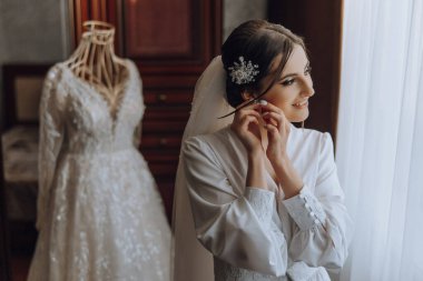 Evdeki düğün töreninden önce güzel genç gelin küpelerini takar. Sabahları beyaz cüppeli bir gelin odasına küpe takıyor..