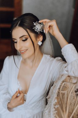 Sabahları beyaz bir bornozla inanılmaz güzel bir gelin ve yatak odasındaki yatakta uzun bir peçe oturuyor. Gelin, düğün töreninden önce poz verir..