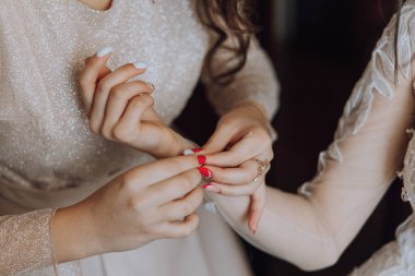 Gelinin sabahı. Bir nedime gelinin kollarındaki düğmeleri bağlamasına yardım eder. Kız arkadaşlar gelinin elbisesini bağlamasına yardım edin.