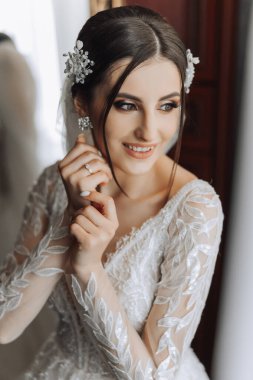 Şık bir gelinlik içinde siyah saçlı ve düğün sabahı odasında çarpıcı makyajlı güzel bir gelinin moda fotoğrafı. Gelin düğün için hazırlanıyor.