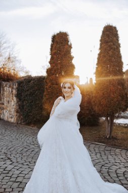 Düğün portresi. Esmer bir gelin, uzun bir peçeyle örtünerek doğada poz veriyor. Güzel makyaj. Dantelli elbise. Gün ışığı. Sonbahar fotoğraf çekimi