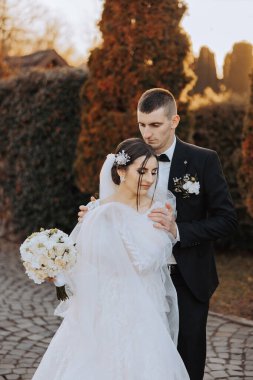 Genç bir gelin ve damat sonbahar güneşinin ışınlarında şefkatle kucaklaşır. Şefkatli ve güzel genç kız gelin. Bir adam sevgilisini öper. Güzel bir bahçenin arka planında