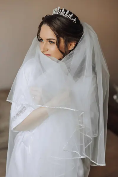 portrait of an incredibly beautiful girl bride in a white robe in the bedroom, the bride poses holding her veil in her hands and covers herself with it.