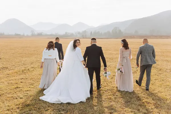 Wedding photo session in nature. The bride and groom are walking in the field with their friends. Happiness. A group of young people. celebration. Autumn wedding. The same clothes
