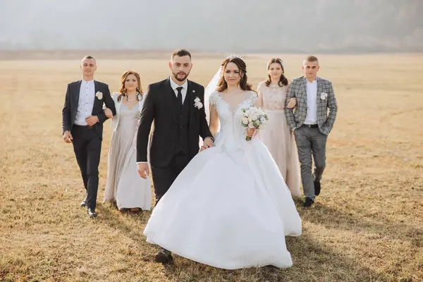 Wedding photo session in nature. The bride and groom and their friends pose against the background of mountains in a field. Happiness. A group of young people. celebration. Autumn wedding. The same clothes