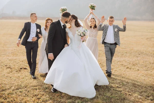 Wedding photo session in nature. The bride and groom and their friends pose against the background of mountains in a field. Happiness. A group of young people. celebration. Autumn wedding. The same clothes