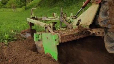 Bir traktör kırsalda toprak yetiştirir. Bir traktör, küçük bir çiftlikte sabanla tarlayı sürüyor. 4K video. Araziyi yakından işlemek için Tiller.