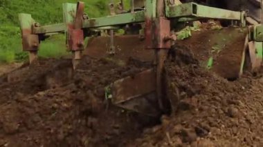 Bir traktör kırsalda toprak yetiştirir. Bir traktör, küçük bir çiftlikte sabanla tarlayı sürüyor. 4K video. Araziyi yakından işlemek için Tiller.