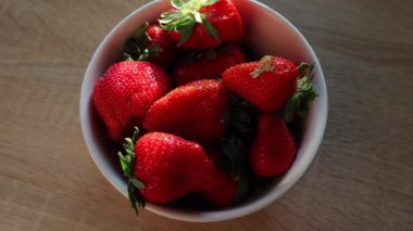 Bir kadın mutfaktaki bir kaseye olgun kırmızı çilekler koyar. Genç bir kadın taze çilekleri elleriyle alır. Sağlıklı atıştırmalıklar, mevsimlik meyveler, beslenme kavramları.