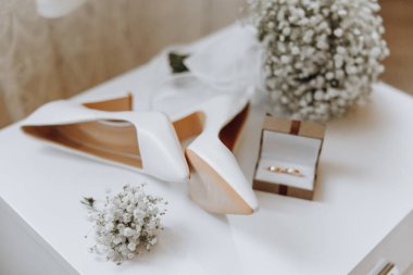 Bir çift beyaz ayakkabı ve beyaz bir çiçek aranjmanı bir masada oturur. Ayakkabılar üst üste konur ve çiçek aranjmanı arka plandadır. Zarafet ve incelik kavramı