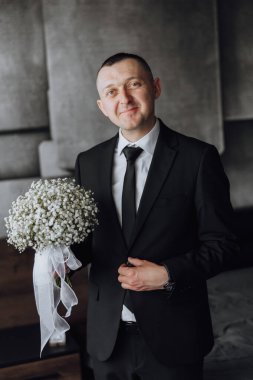 Takım elbiseli ve kravatlı bir adam elinde bir buket beyaz çiçek tutuyor. Zarafet ve entelektüellik kavramı. Çünkü adam resmi giyinmiş ve elinde narin bir buket tutuyor.