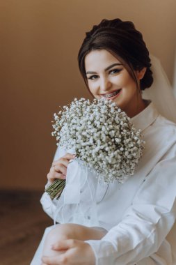 Bir kadın oturuyor ve elinde bir buket beyaz çiçek tutuyor. Gülümsüyor ve mutlu.