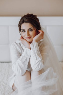 Beyaz çarşaflı ve peçeli bir kadın yatakta oturuyor. Beyaz bir elbise giyiyor ve elleri dizlerinin üzerinde. Zarafet ve incelik kavramı