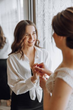 İki kadın birbirine gülümsüyor. Bir tanesi beyaz gömlek ve siyah elbise giyiyor.