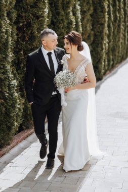 Bir adam ve bir kadın yolda yürüyorlar, adam takım elbise ve kravat takıyor.