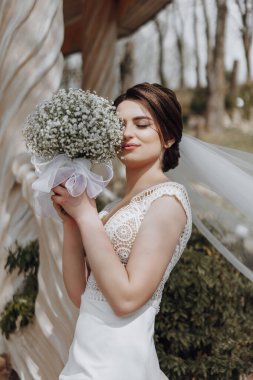 Güzel gelin elinde bir buket çiçek tutuyor ve doğada poz veriyor.
