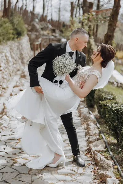 a man in a business suit and a woman in a white dress in nature. The groom hugs and kisses the bride