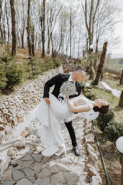 a man in a business suit and a woman in a white dress in nature. The groom hugs and kisses the bride