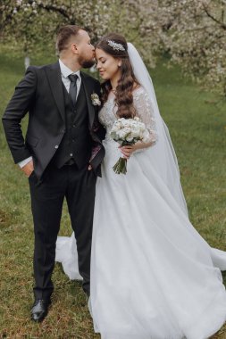 Gelin ve damat bir tarlada duruyorlar, gelin bir buket çiçek tutuyor. Gelin beyaz bir elbise giyiyor ve damat bir takım elbise giyiyor. Sahne mutlu ve romantik.