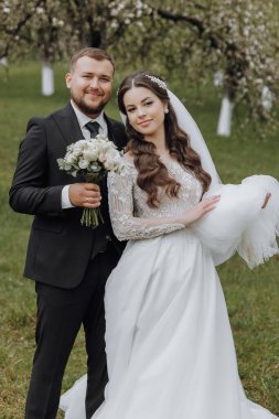 Bir gelin ve damat tarlada fotoğraf çektirmek için poz veriyorlar. Gelin bir buket tutuyor ve damat da bir buket tutuyor.