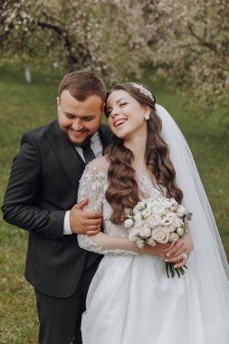 Bir gelin ve damat tarlada fotoğraf çektirmek için poz veriyorlar. Gelin elinde bir buket çiçek tutuyor.