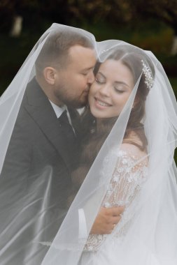 Yakışıklı ve şık bir damat gelinini duvağının altında beyaz bir elbiseyle kucaklıyor.