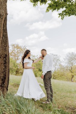 Gelin ve damat bir tarlada duruyorlar, gelin damadın yüzüne dokunuyor. Sahne huzurlu ve romantikti. Çift, güzel bir açık hava ortamında birlikte vakit geçiriyordu.