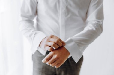 Beyaz gömlekli bir adam gömleğinin kollarını düzeltiyor. Formalite anlayışı ve detaylara dikkat. Çünkü adam gömleğinin düzgün bir şekilde giydirildiğinden ve kollarının güzelce kıvrıldığından emin olmak istiyor.