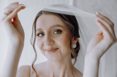 Bir kadın yüzünde bir peçe tutuyor, gülümsüyor. Mutluluk ve kutlama kavramı. Kadın büyük ihtimalle düğün ya da fotoğraf çekimi gibi özel bir olaya hazırlanıyor.